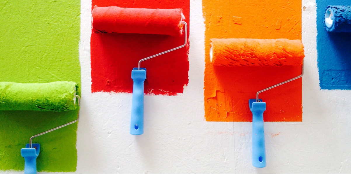 Photo of paint rollers painting colourful stripes on a white wall